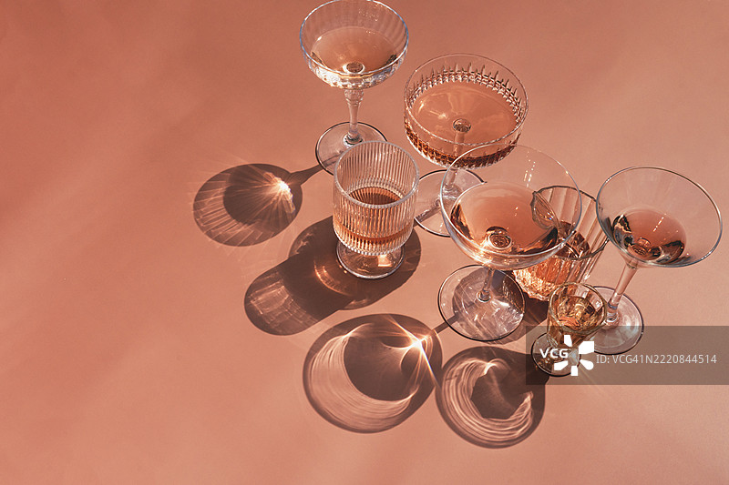几种不同的鸡尾酒或无酒精鸡尾酒杯，盛着玫瑰酒，桌面上有明显的阴影。俯视角度。图片素材