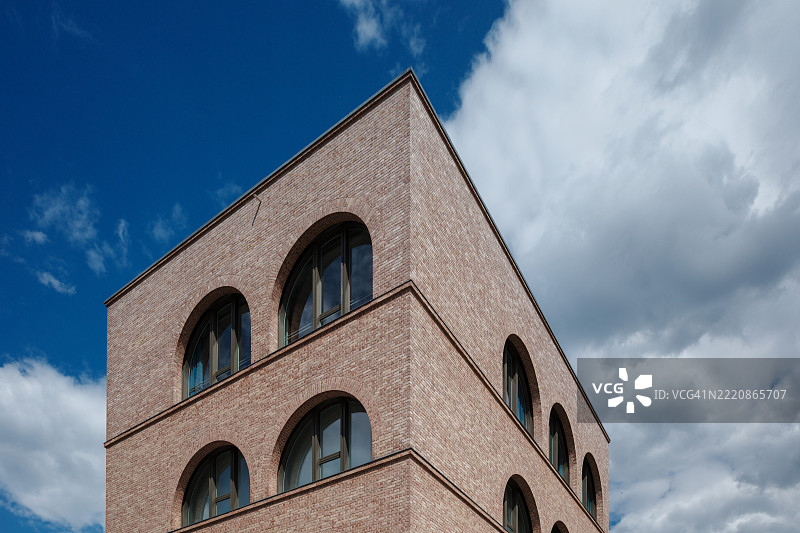 一座现代建筑，采用浅红棕色砖块，具有独特的设计，配有多个拱形窗户。图片素材
