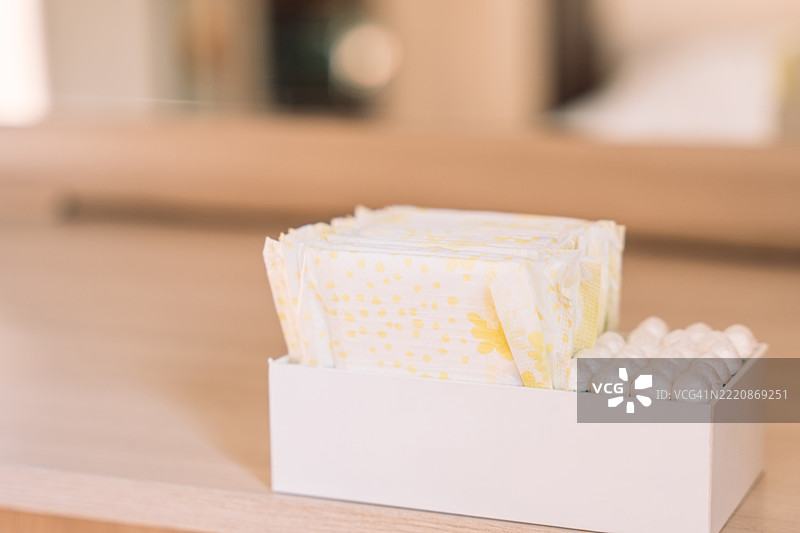 放置在镜子旁的卫生巾和棉条盒，放在浅色木架上。自然光和整齐的摆放传达出日常个人护理和卫生习惯。图片素材