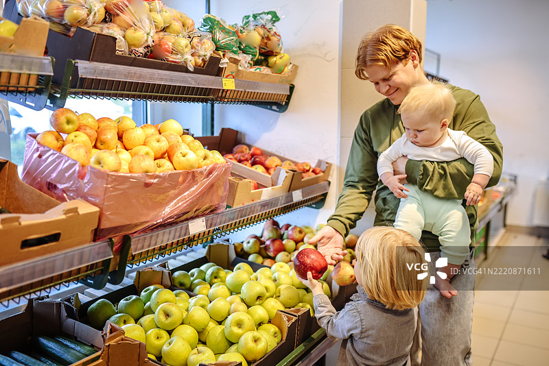 带着孩子购物：爸爸在商店里为幼儿挑选水果图片素材