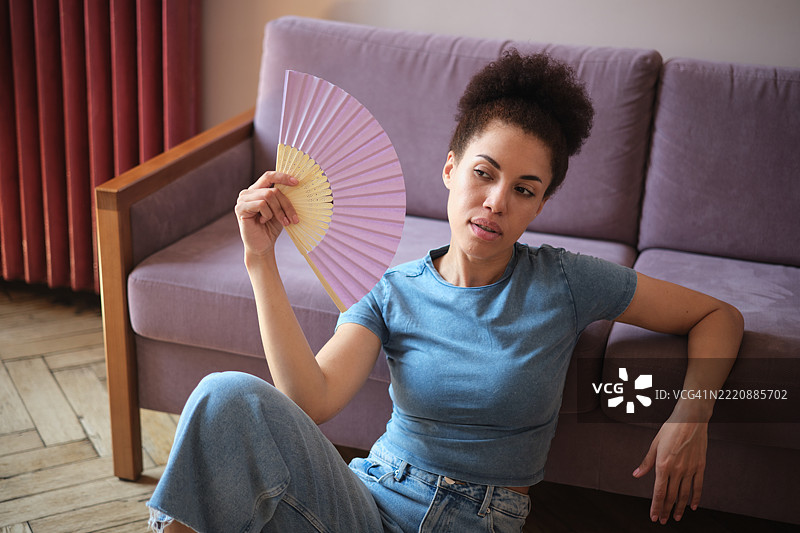 夏季炎热。疲惫的年轻非裔美国人在家中用纸扇降温。图片素材