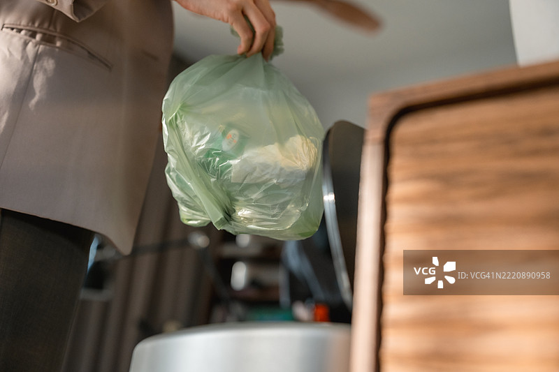 女商人系好一个装满垃圾的袋子，并将其放入厨房垃圾桶，然后准备出门上班。图片素材