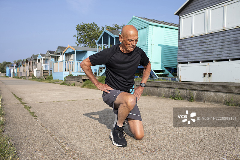 活跃的老年男性在海滩小屋旁的步道上做热身运动图片素材