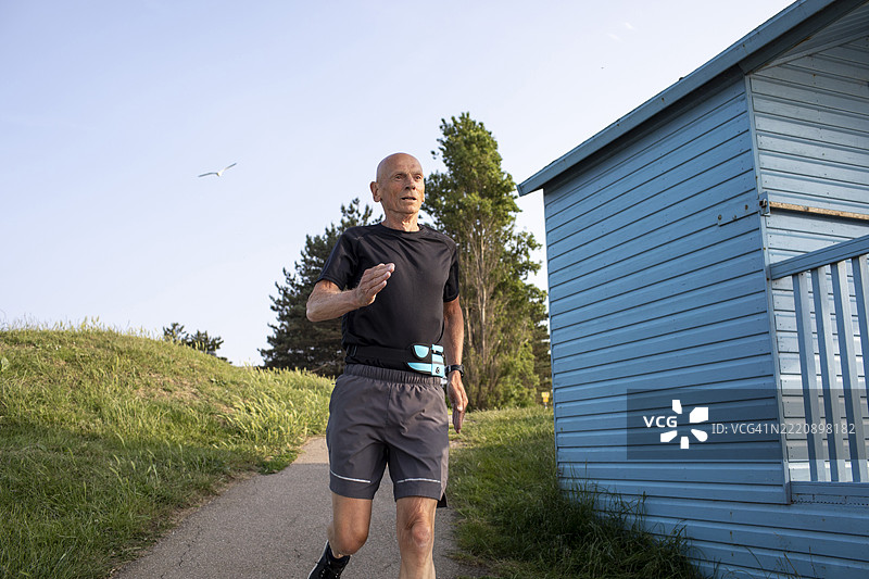 活跃的老年男子在海滩小屋旁奔跑下坡图片素材