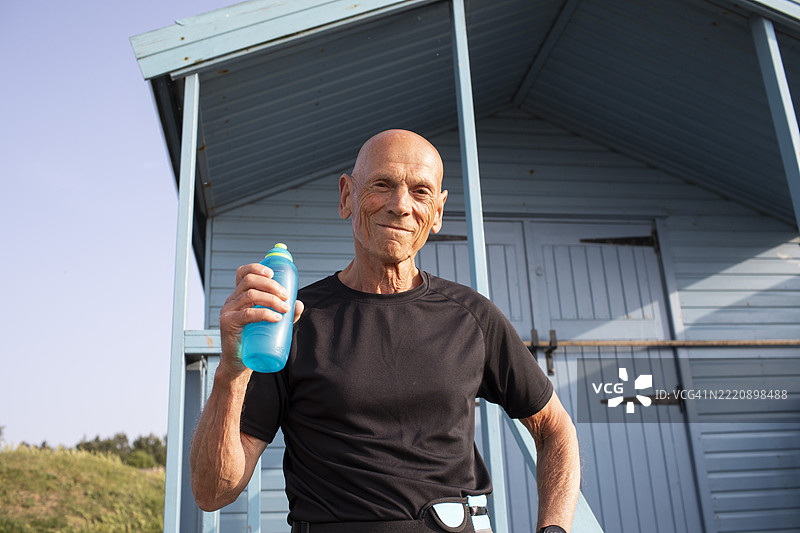 积极活跃的老年男子在海滩小屋旁拿着水瓶图片素材