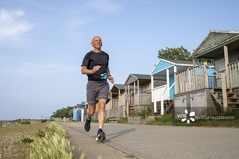 一位活力四射的老年男子在一排海滩小屋旁跑步，视角从低处拍摄。图片素材