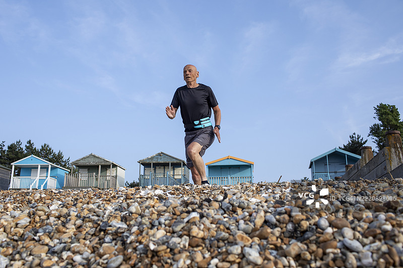 活跃的老年男子在海滩小屋附近的卵石海滩上奔跑图片素材