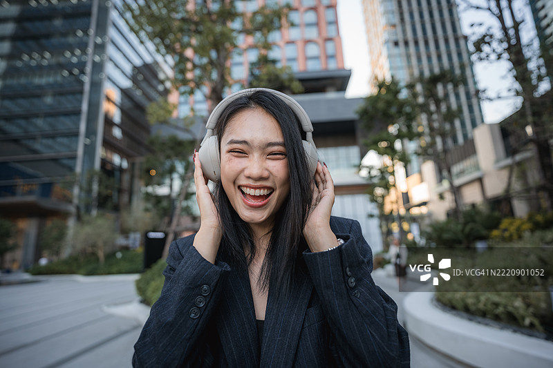 亚洲女商人在高楼大厦和繁忙城市中，沉浸在无线耳机音乐中的肖像照图片素材