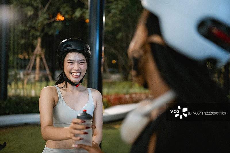 快乐的女性在夜骑结束后把水瓶递给她的朋友们图片素材