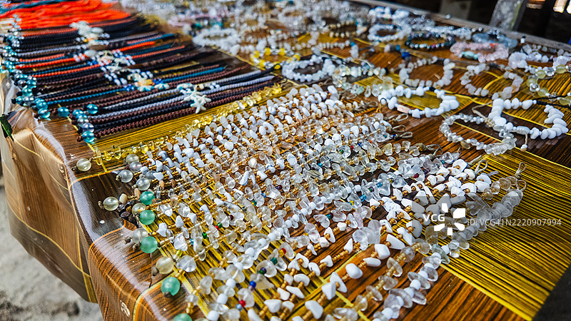 市场桌上摆放着由贝壳、珠子和石头手工制作的五彩斑斓的项链和手链特写。图片素材