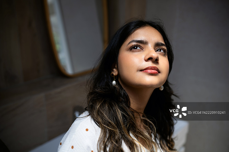 一位年轻的印度裔女性在柔和的自然光中，深思地仰望着天空。图片素材