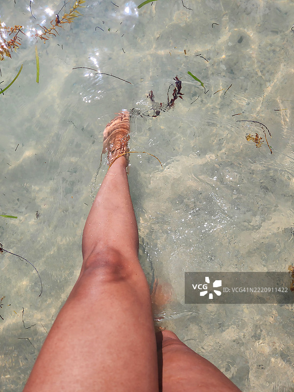 在海滩水边站着的西班牙裔女性，一只脚浸入水中。图片素材