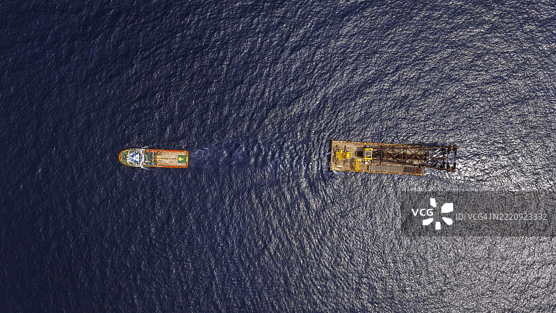 航拍视角的拖船拖曳着一艘载有石油钻井平台的驳船。图片素材
