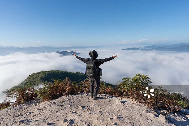 一名男子站在山顶，晨光中俯瞰云海。图片素材