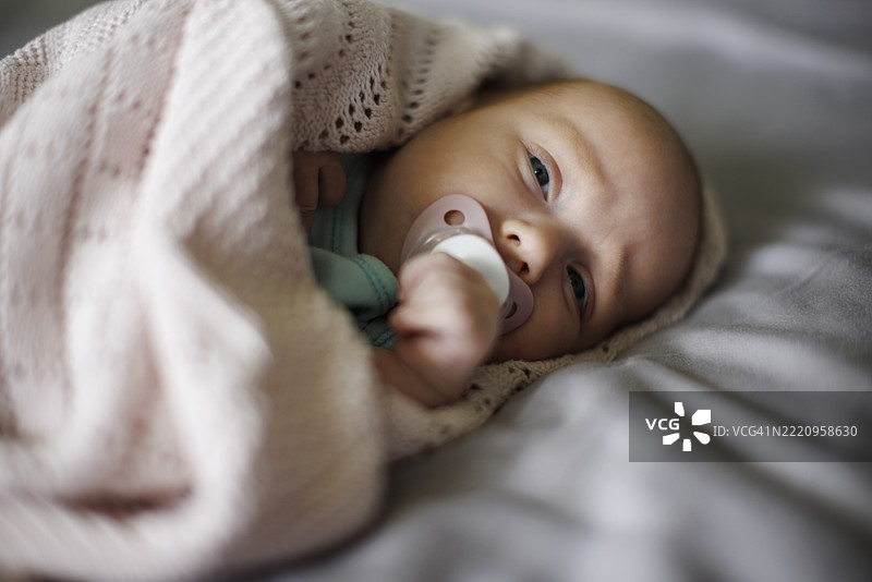 新生儿被柔软的毯子包裹，躺在床上，嘴里含着安抚奶嘴图片素材