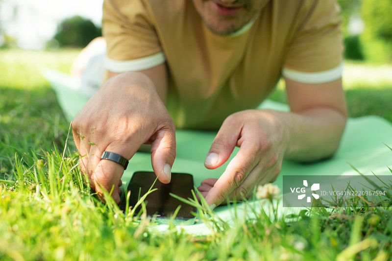 戴着智能戒指的男子在户外练习瑜伽时查看智能手机图片素材