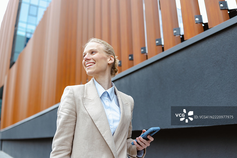 职业女性在户外自信地微笑着，手持智能手机。图片素材