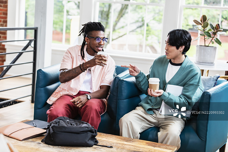 两名男子在共享办公空间的大厅里喝咖啡交谈。图片素材