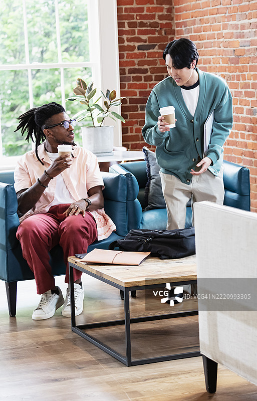 两名男子在共享办公空间的大厅里喝咖啡交谈。图片素材