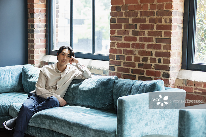 坐在窗边沙发上的亚洲男子，沉思不已图片素材