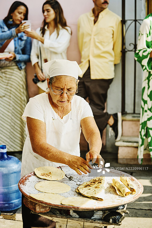 中景镜头，老年女性在烤架上烹饪自制墨西哥菜。图片素材