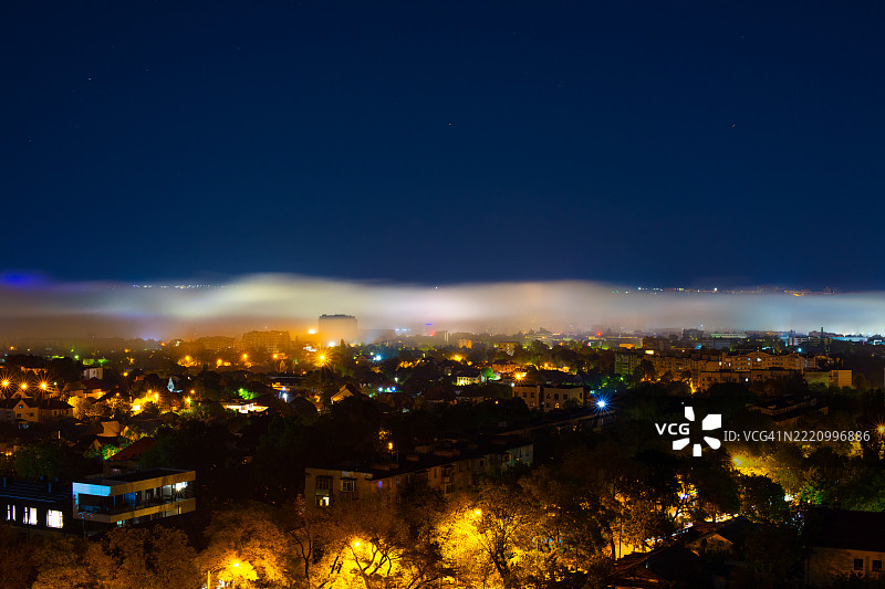 夜晚的城市景观在清澈的蓝色夜空下，雾蒙蒙的地平线中闪烁着灯光图片素材