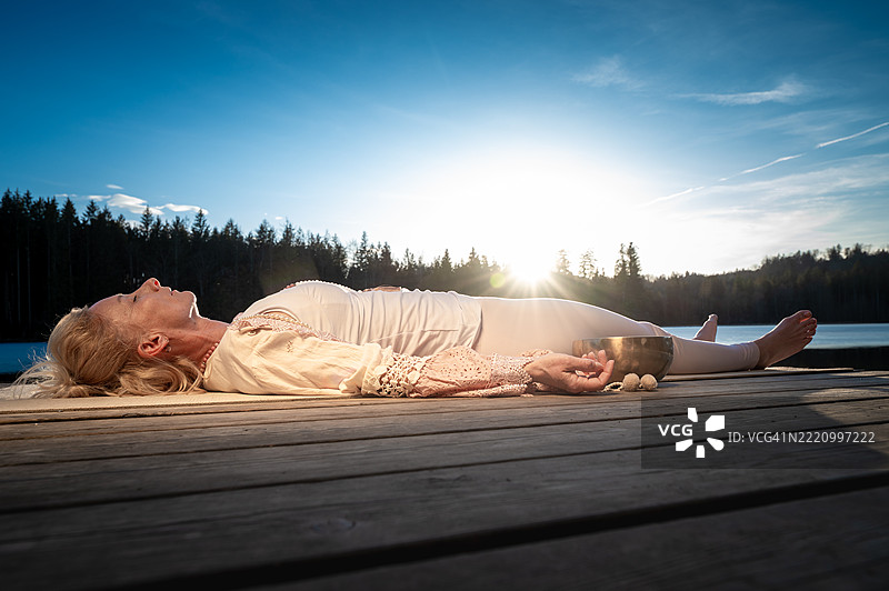中年女性在山湖的码头上练习瑜伽图片素材