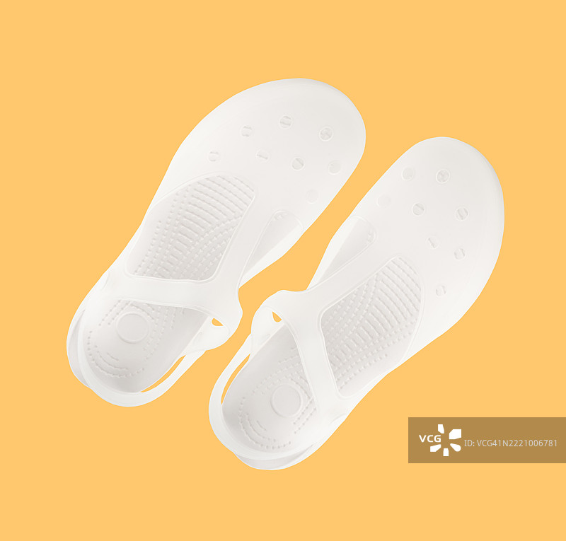 一双白色凉鞋放在黄色背景上。图片素材