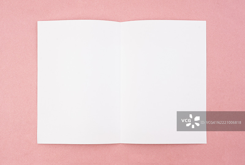 在粉色背景上展开的空白折叠白色A4纸张。图片素材