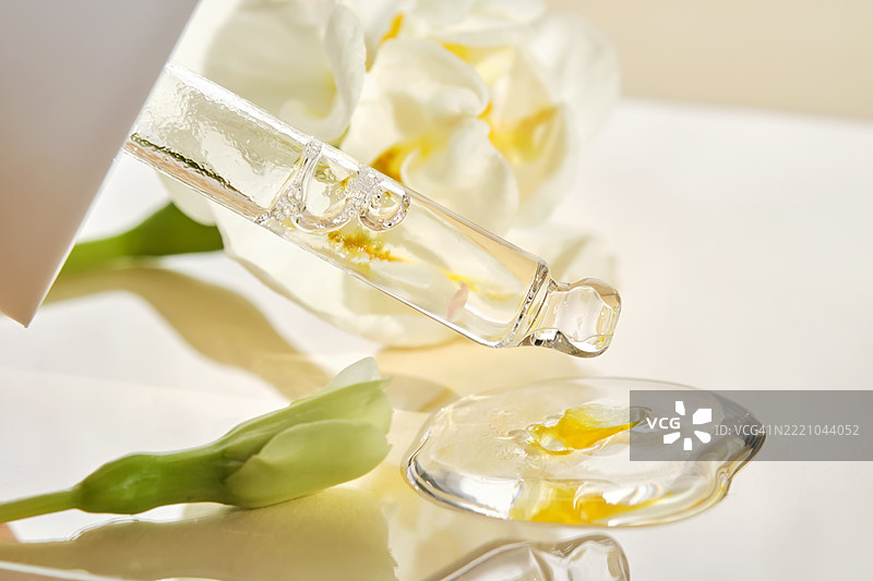 一滴血清在米色背景的白色花朵中。图片素材