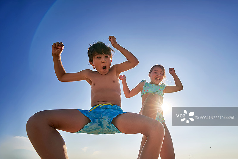 一个男孩和一个女孩在蓝天的背景下享受海滩的乐趣。图片素材