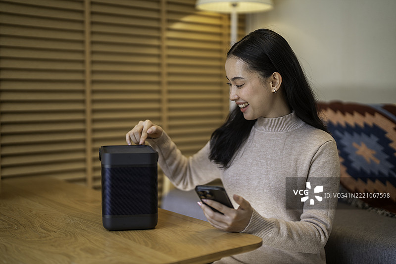 年轻女性在家中使用便携式蓝牙音箱图片素材