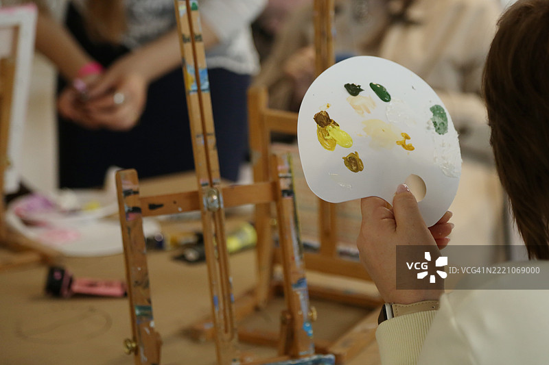 艺术家的调色板上有多种颜色的水粉颜料，背景是模糊的工作室内部。图片素材