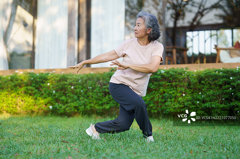 一位活跃的退休老年女性在柔和的晨光中，在前院练习太极。图片素材