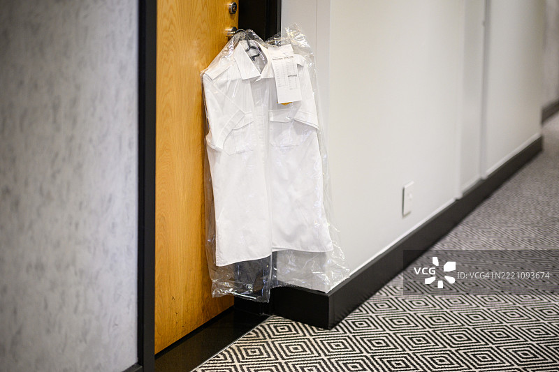新洗的白衬衫用塑料包装挂在酒店房间门上，背景是有图案的地毯走廊。图片素材