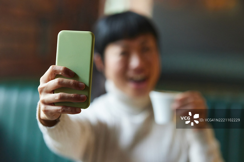 在咖啡馆里，一位女性用手机拍摄自拍照的特写。图片素材