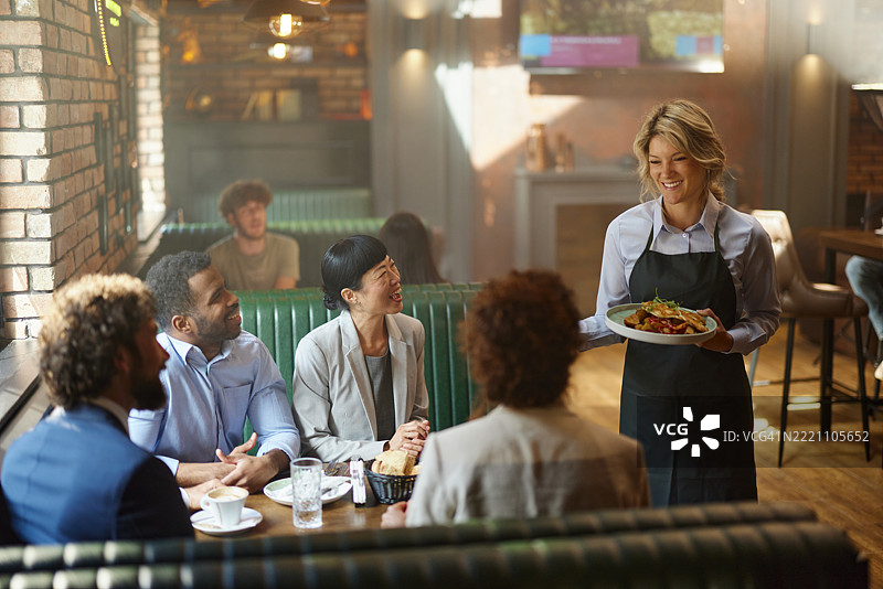 快乐的女服务员在餐厅为商务人士上菜。图片素材