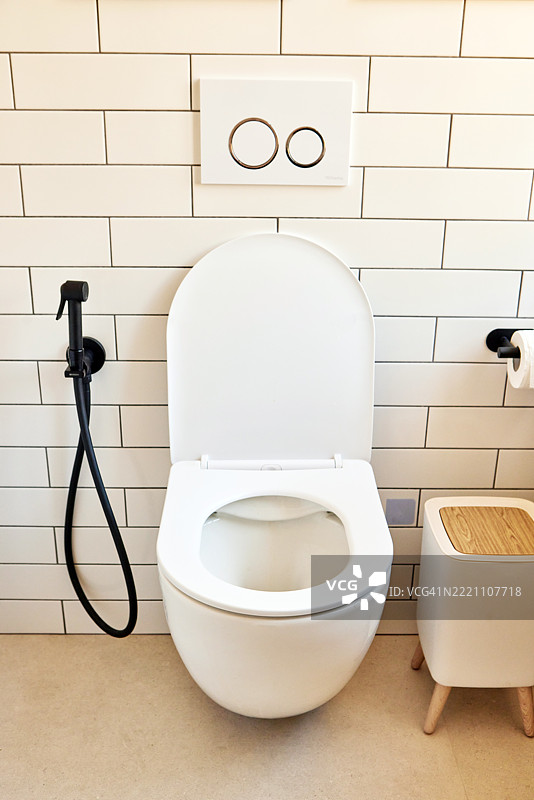 现代卫生间中的现代马桶，配有白色瓷砖和喷头淋浴。图片素材