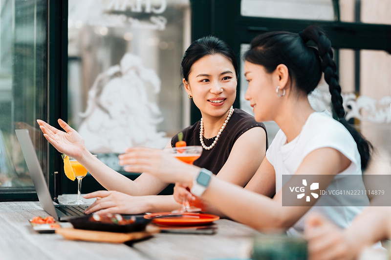 两位年轻亚洲女商在咖啡馆侧面交谈，享受咖啡休息时间。现代职场中的女性领导力。通过科技保持商业联系。商业管理。远程工作。图片素材