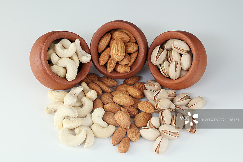 开心果、杏仁和腰果从陶罐中洒落出来图片素材