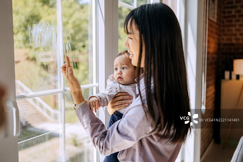 女人一边担心地检查脏窗户，一边抱着小女孩。图片素材