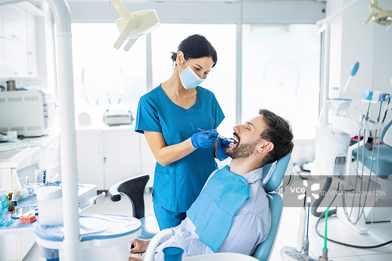 女牙医在常规牙科检查中为患者检查牙齿图片素材