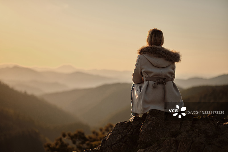 一位女性坐在山顶的岩石上，背影。图片素材