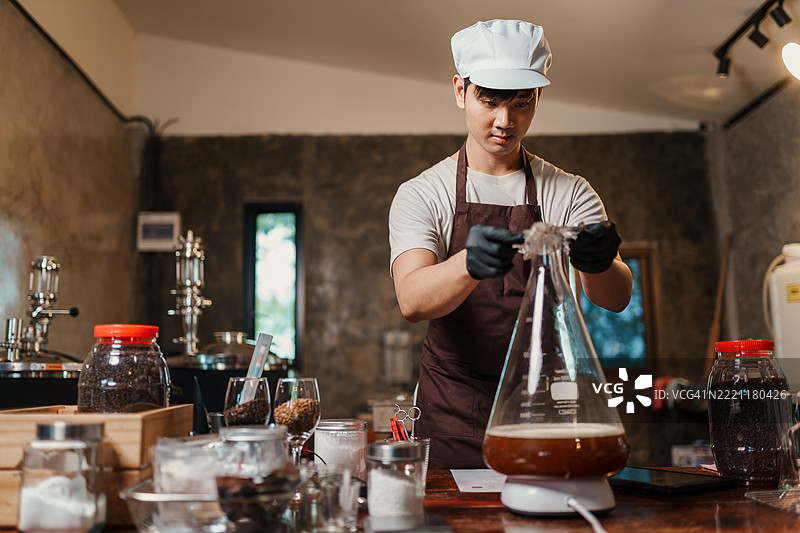 一名家庭酿酒师在准备酵母培养液时，用铝箔封住实验室烧瓶，穿着手套和围裙，专注于酿造过程中的清洁。图片素材