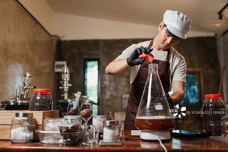 亚洲家庭酿酒师在实验室烧瓶中准备酵母 starter，穿着围裙和手套，专注于啤酒酿造过程中的精确操作。图片素材