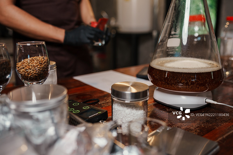实验室烧瓶中酵母启动液在磁力搅拌器上旋转的特写，桌上摆放着酿酒原料和设备，展示了手工啤酒酿造过程。图片素材