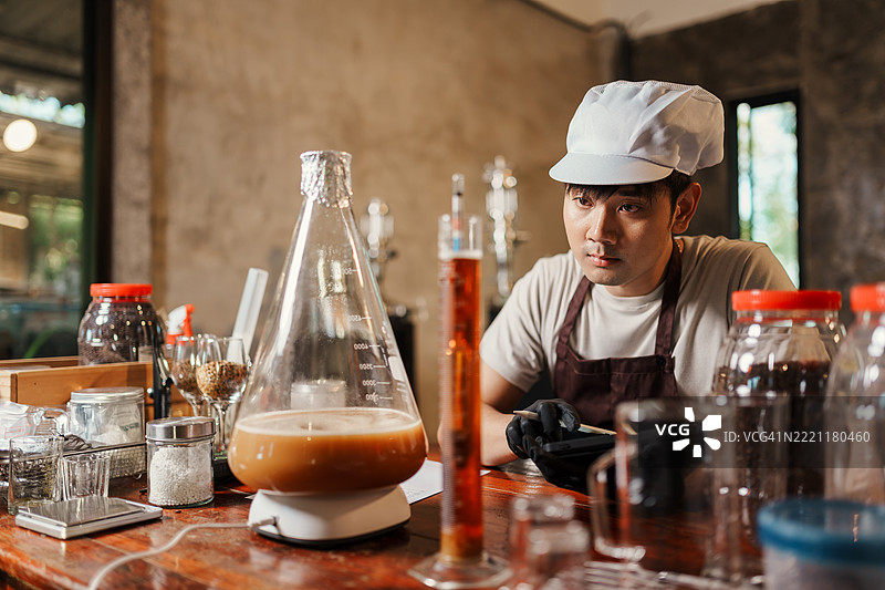 亚洲家庭酿酒师观察酵母培养液和比重计样本，专注于手工啤酒酿造过程中的发酵质量控制。图片素材