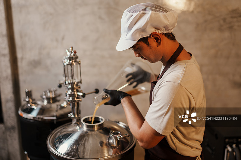 亚洲家庭酿酒师小心地将酵母启动液加入发酵罐，确保精酿啤酒的质量和一致性。图片素材