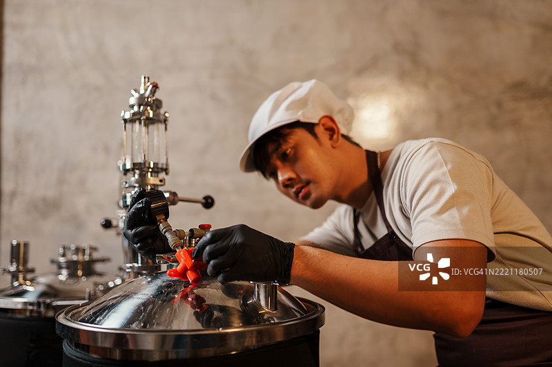 亚洲家庭酿酒师在发酵罐上调整阀门，仔细控制工艺啤酒酿造过程中的压力和气体流量。图片素材