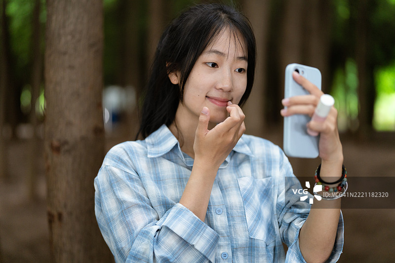 年轻女性在森林中涂抹口红，休闲风格，自然氛围图片素材